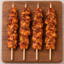 Four cooked Portuguese chicken kebabs with red spice seasoning and light char, arranged on a wooden serving board.