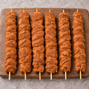 Six raw XL oregano chicken kebabs on wooden skewers arranged vertically on a rustic wooden board.
