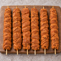 Six raw XL oregano chicken kebabs on wooden skewers arranged vertically on a rustic wooden board.