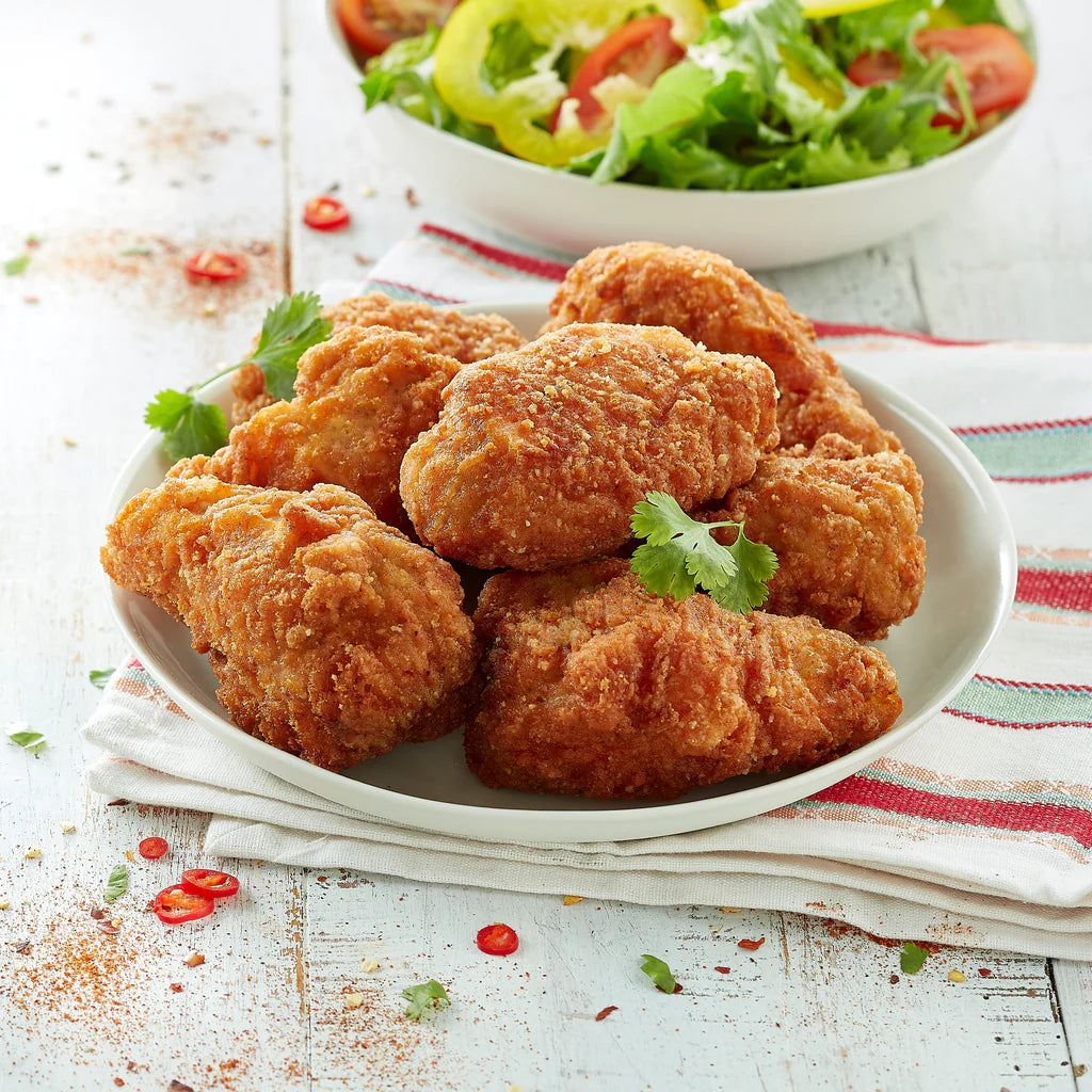 Cooked Ingham’s Devil Chicken Wing Dings on a white plate with herb garnish and salad in the background; serving suggestion.