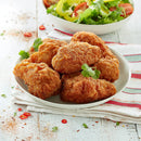 Cooked Ingham’s Devil Chicken Wing Dings on a white plate with herb garnish and salad in the background; serving suggestion.