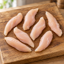 Fresh raw chicken tenderloins spaced on a rustic oak board.